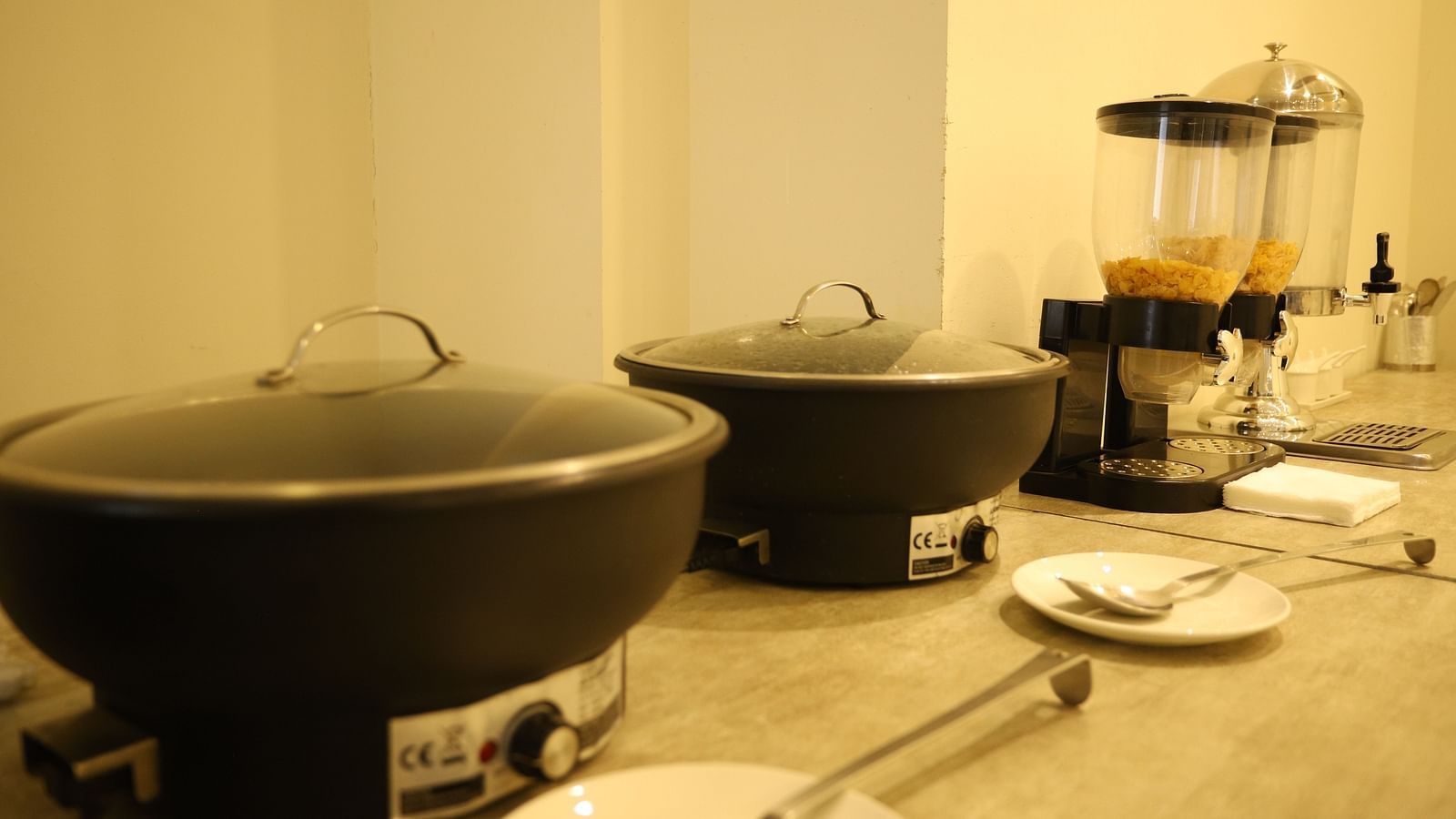 A close-up of a buffet setup shows large black serving dishes and various food items on a counter - Asian Suites Cyber Park, Gurgaon