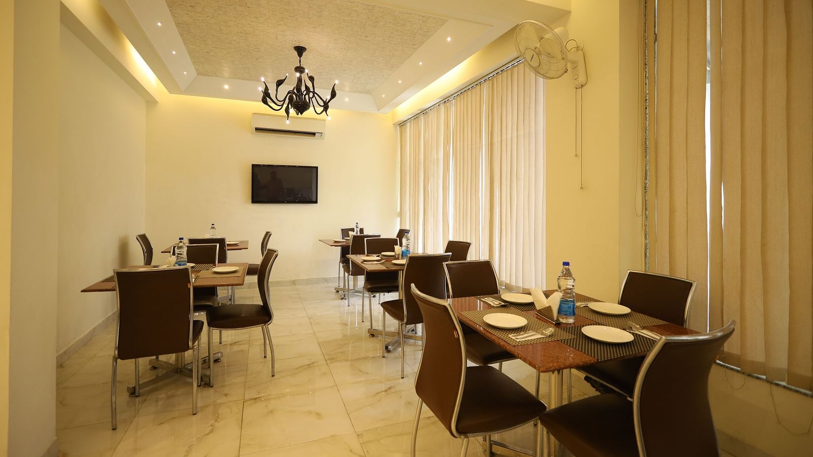 A well-lit dining space with several tables and chairs is decorated with sheer curtains and a chandelier - Asian Suites Cyber Park, Gurgaon