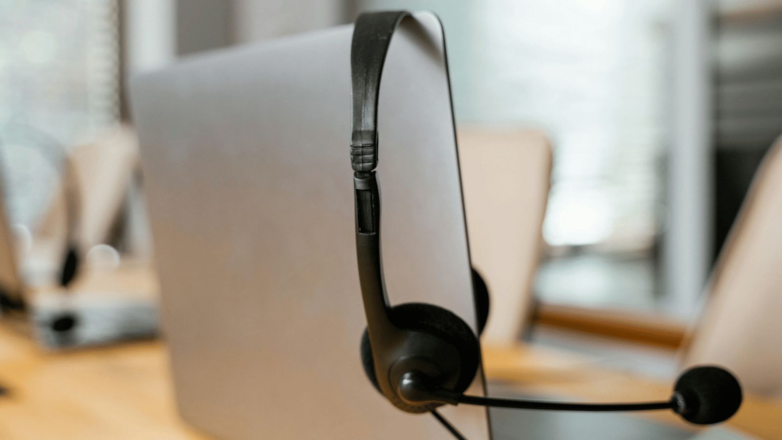 Black headset with microphone hanging on the corner of a laptop screen in an office setting.