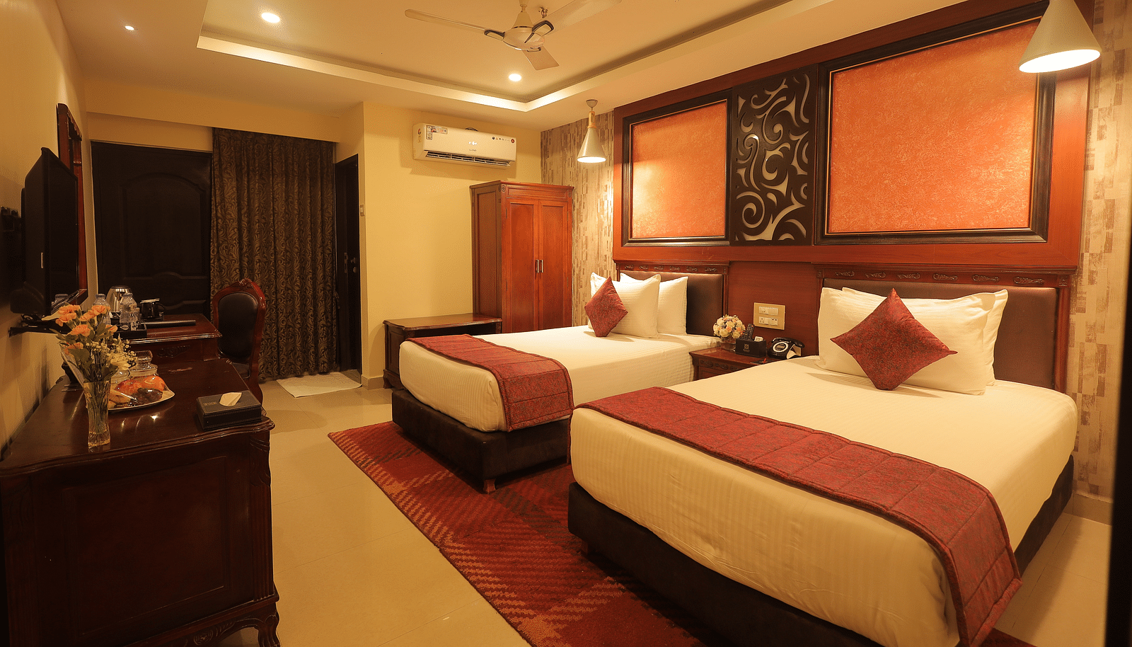 An image of a twin beds with bedside table, a set of table and chairs, flat TV screen, and AC - Sathyam Grand Resort