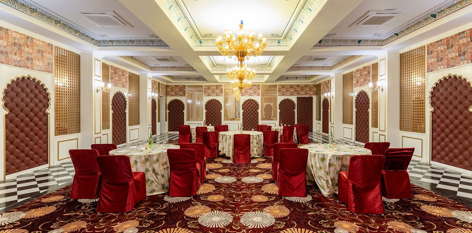 Luxurious banquet hall with red chairs and ornate ceiling at Kesar Bagh Palace.
