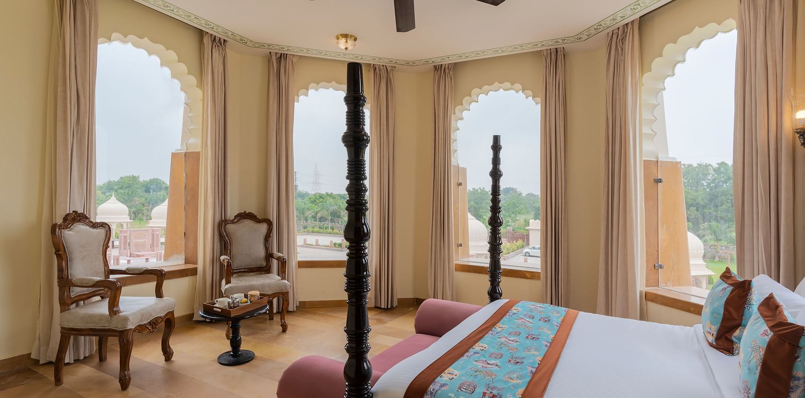 Elegant bedroom with arched windows overlooking scenic landscape at Kesar Bagh Palace.