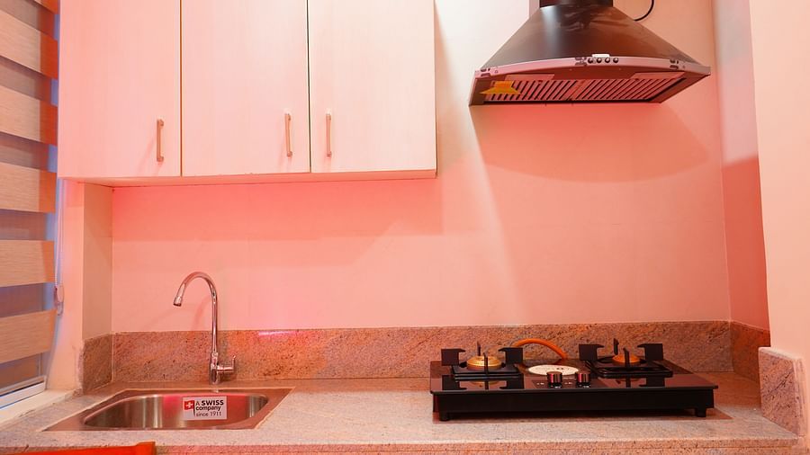A kitchen space with a cooking stove, a chimney, a sink and storage cabinets - A M Suites