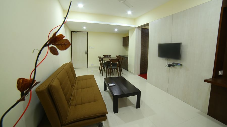 Mysore Gate Hotel, Bangalore Bengaluru A living space featuring a TV a sofa a table and a dining area - Myore Gate Hotel Bangalore