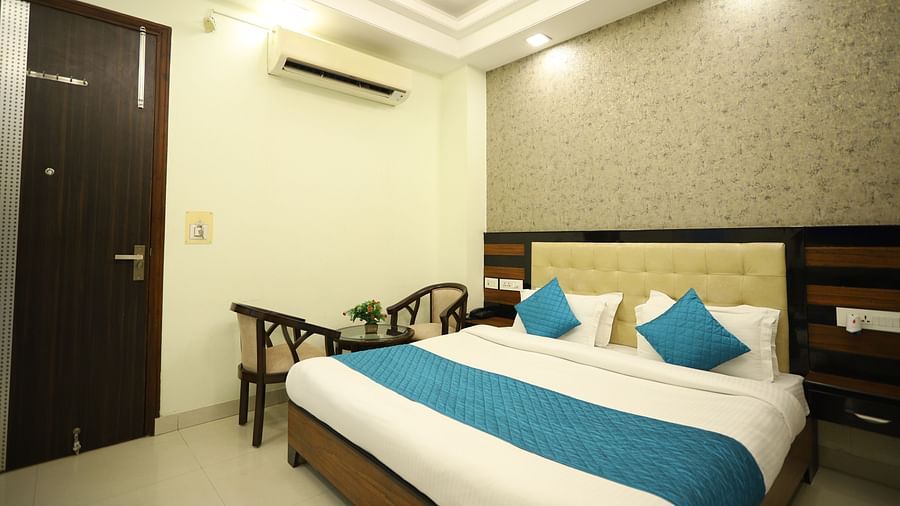 A comfortable room features a double bed with blue and white bedding, wooden furniture, and an air conditioning unit - Asian Suites Cyber Park, Gurgaon