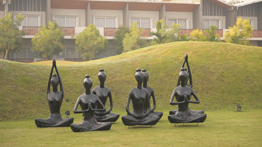 Large meditation-themed sculptures displayed on a green lawn with Hotel Sonar Bangla Mayapur building in the background.