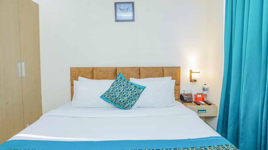 A hotel room with a double bed, blue and white bedding, and light blue curtains - Hyphen Grand, Haridwar