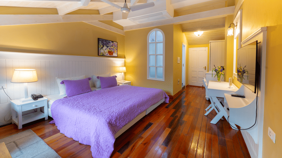 A premium bedroom featuring a bed with purple linens, warm yellow walls, and a white vanity - Johnson Lodge & Spa, Manali