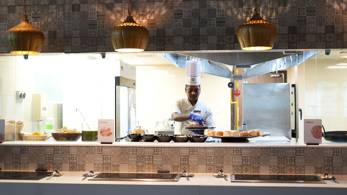 Wide-angle view of the kitchen area where a chef is preparing food at The Residency Towers Rameswaram.
