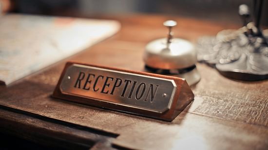 A close up shot of a reception desk with a reception sign and a small concierge bell