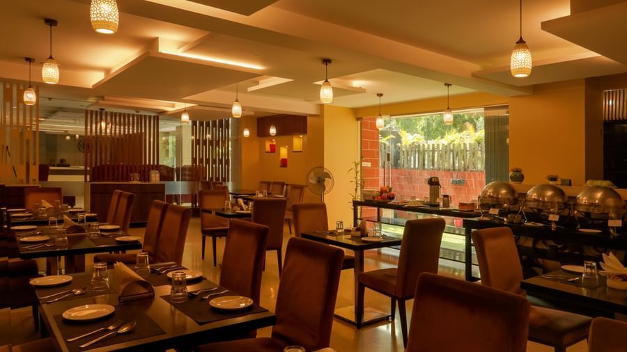 Amara restaurant featuring chairs and tables which have plates, cutlery, glass and napkin. The area is lit with dim lights which are hanging from the ceiling.