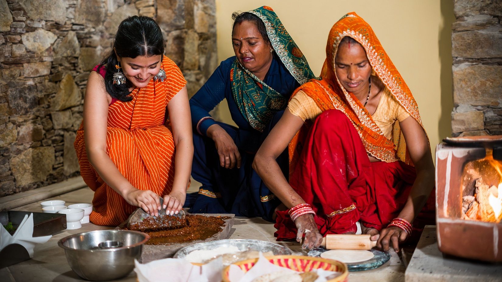 An image of three women in the kitchen, where one is cooking, one is grinding condiments, one woman is making roti- Juna Mahal Jungle Resort, Ranthambore