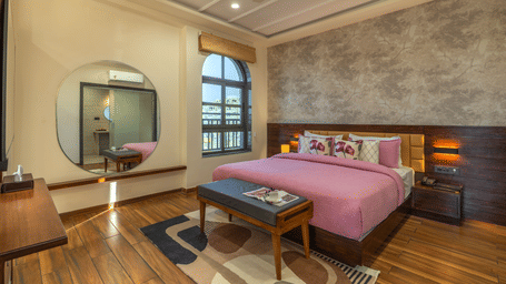 A room with a king size bed, mirror, table, chair, bench, and wall decor inside the room at Perfectstayz Premium Udaipur By The Lake.