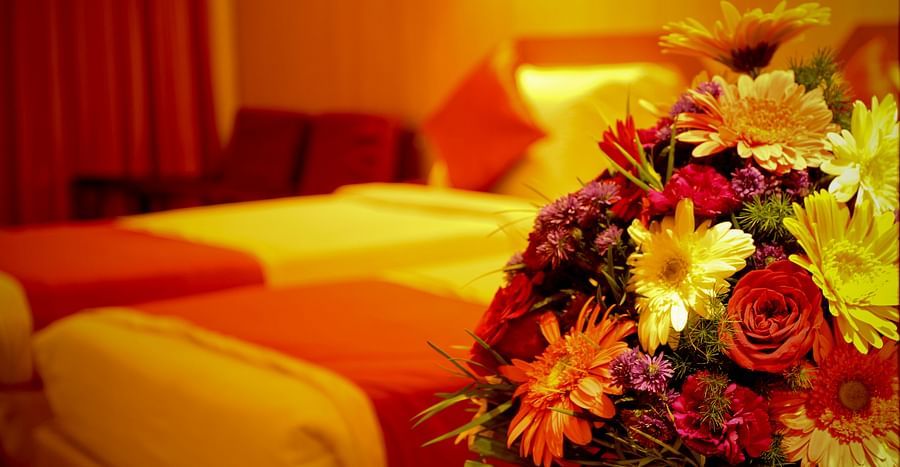 alt-text  Hotel Yasodha Towers - Shallow depth of field closeup shot of a bouquet of flowers with a double bed in the background
