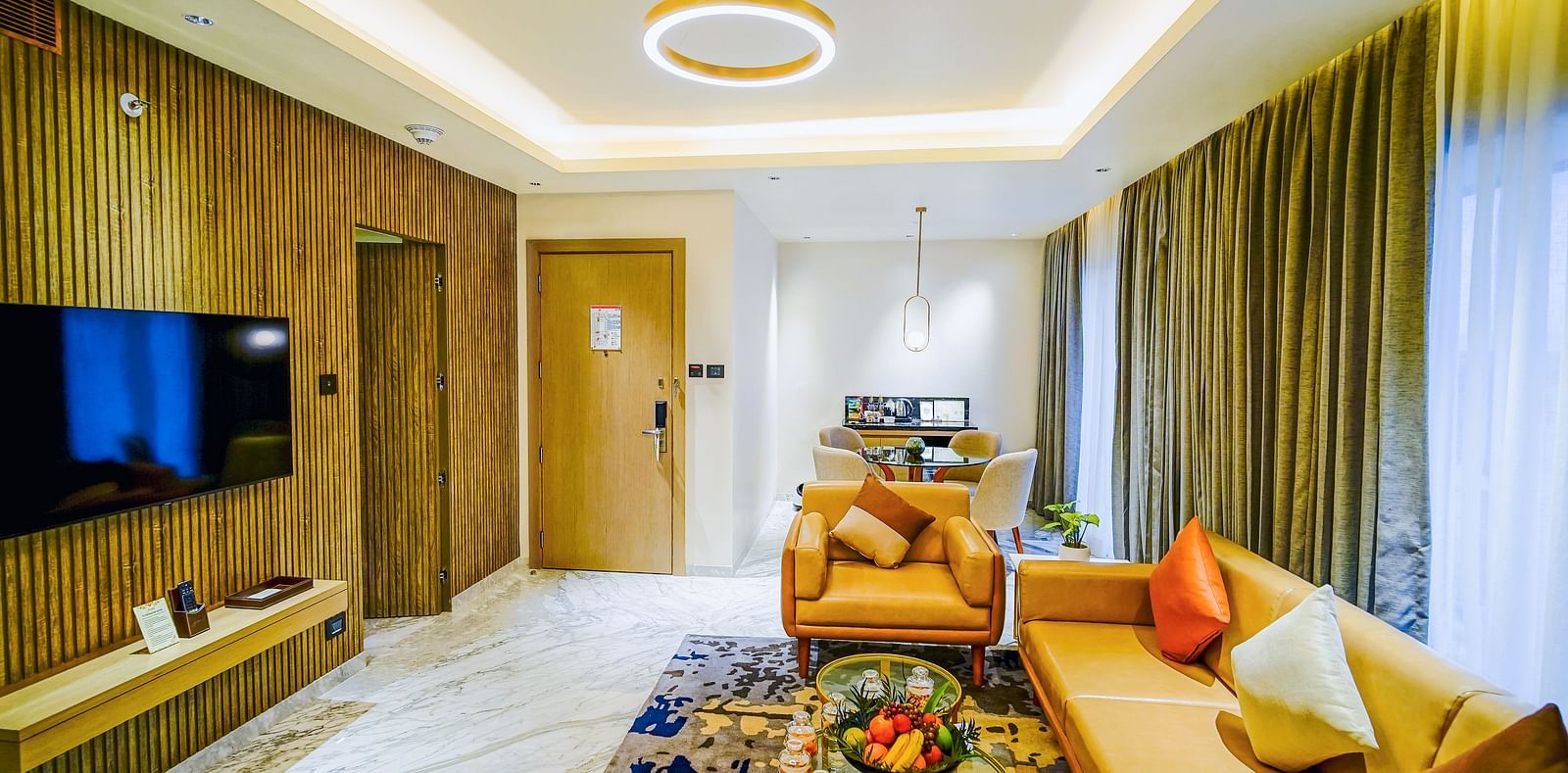 An image of the living room in suite in Madurai filled with amenities like couches, a coffee table, and a wall-mounted televison
