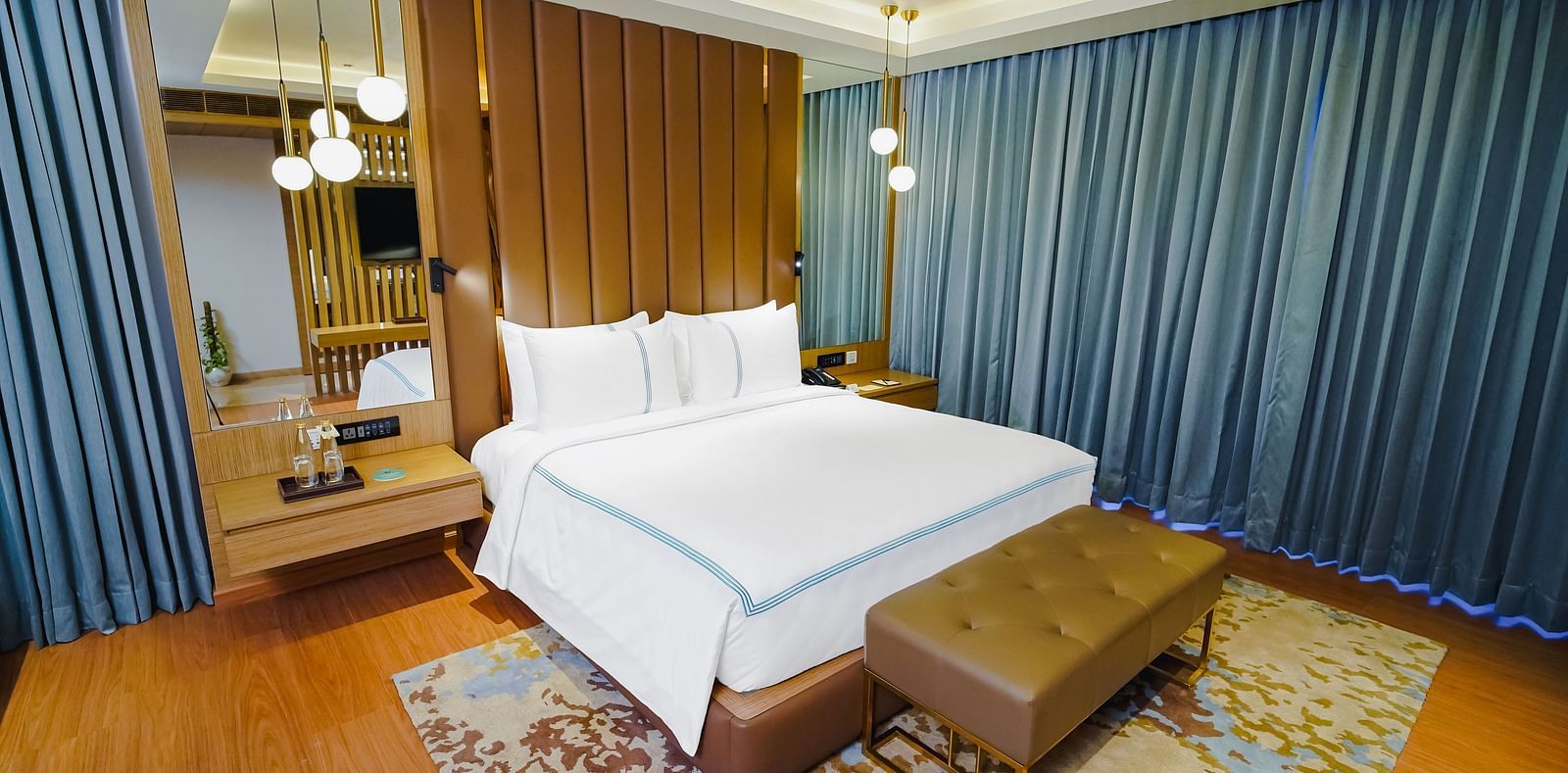 An image of a large bed with a leather bed runner placed under lamps hanging from the ceiling