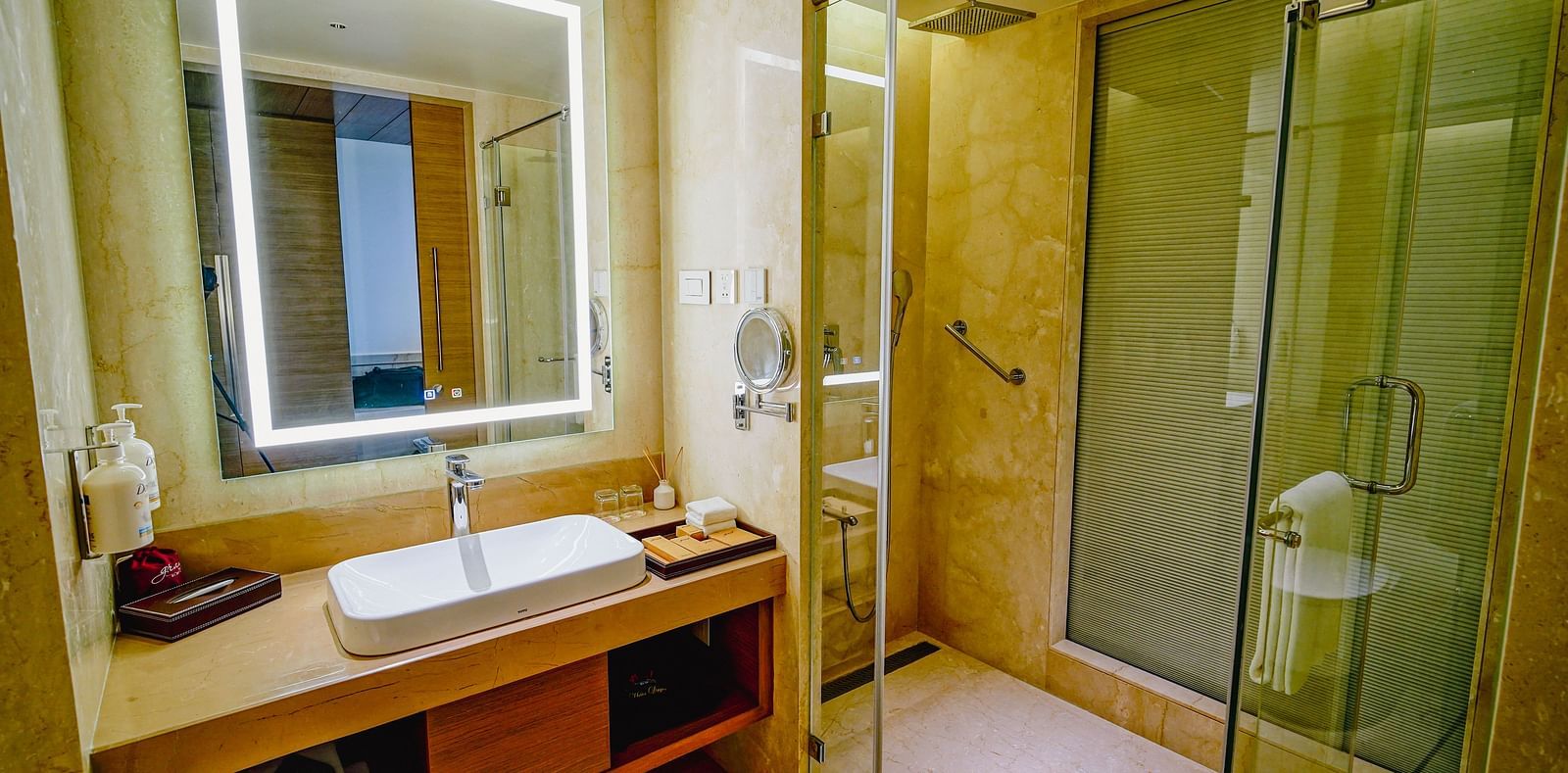 An image of a washroom in our Grand Club room with a large wall-mounted mirror, a sink and a separate shower cuibicle
