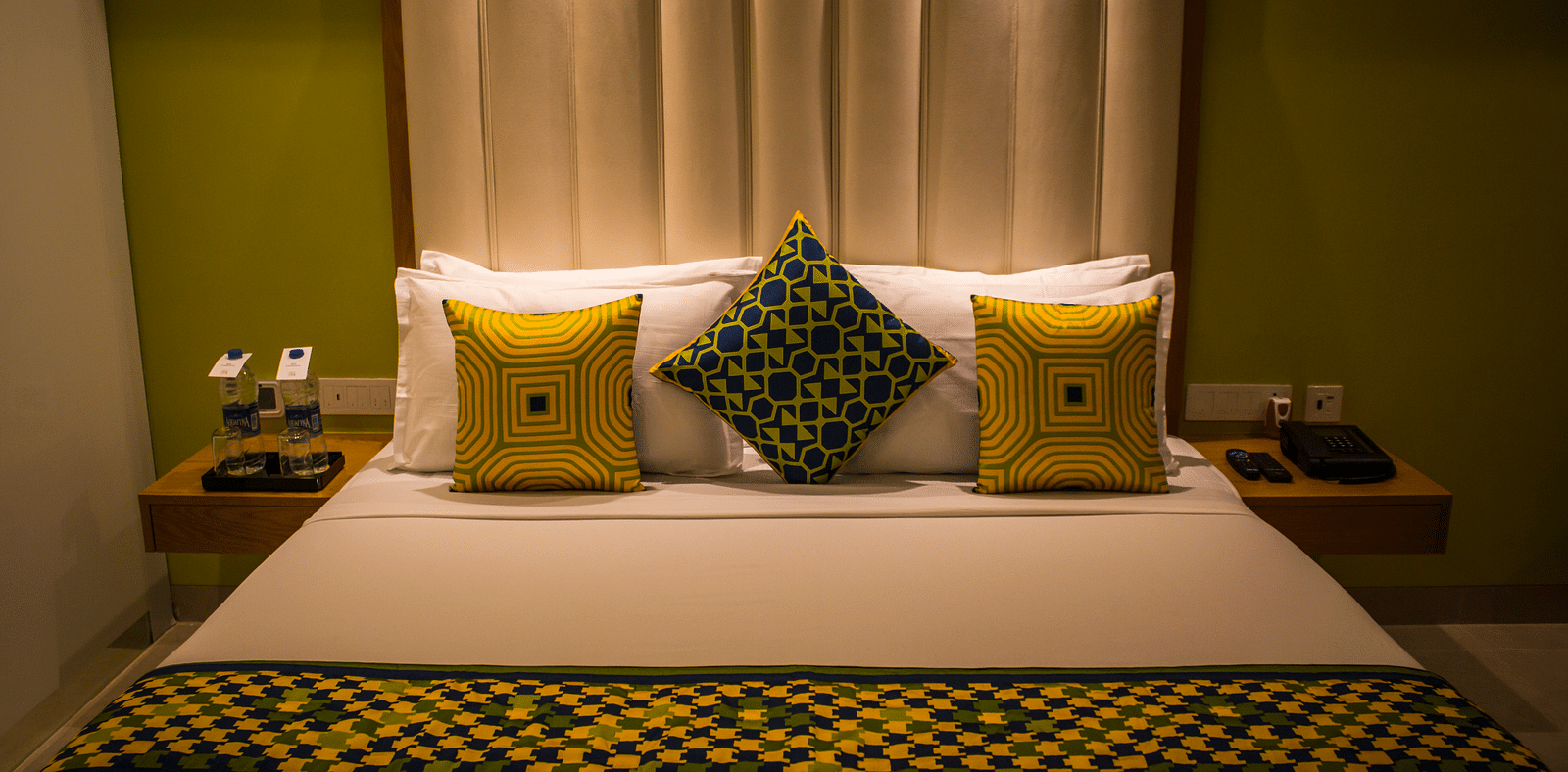 A room with a bed and  pillows arranged on it  along with  a side tables | Regency Tirunelveli By GRT Hotels