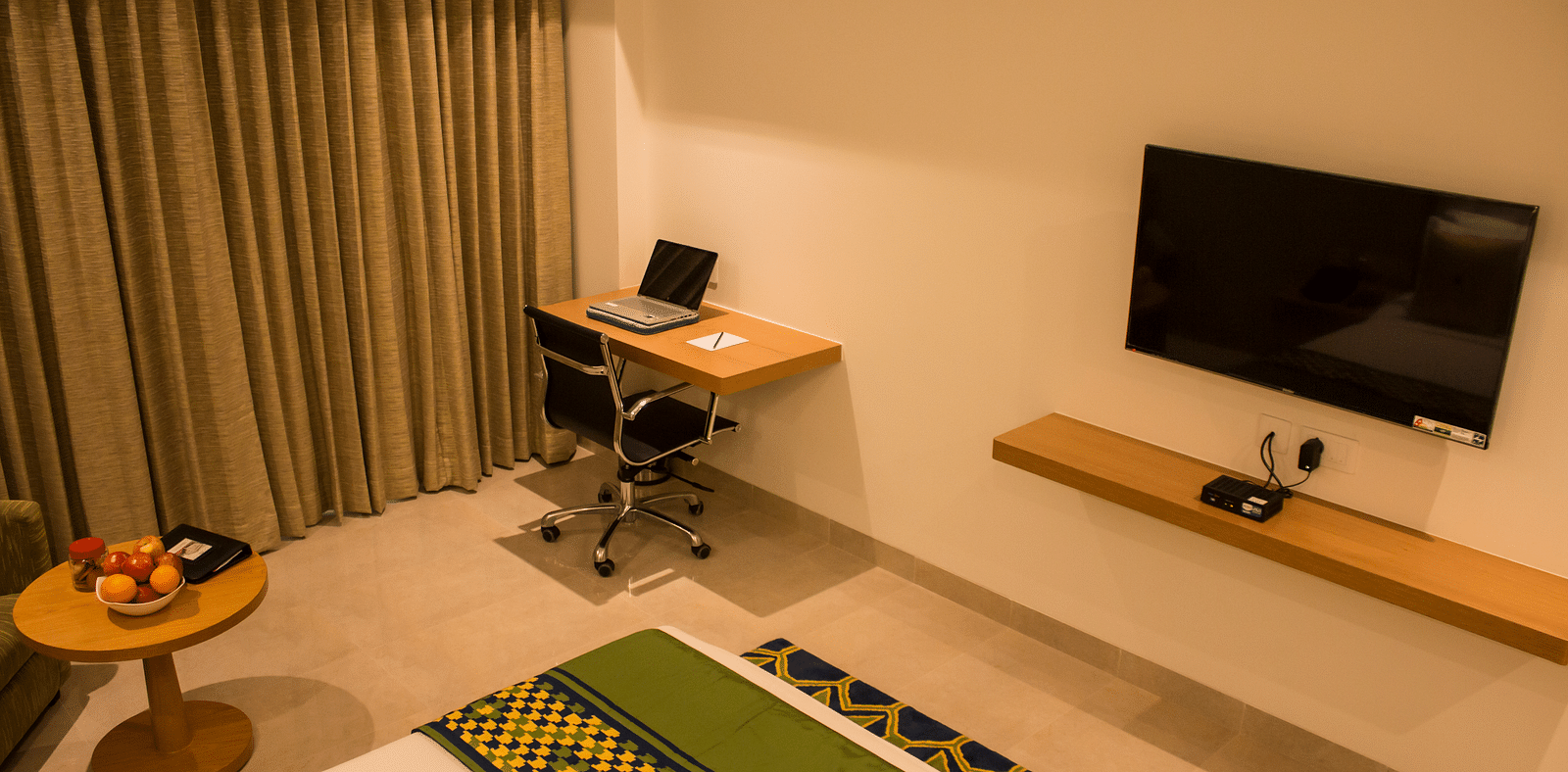 Side view of a room with a bed and  pillows arranged on it  along with  a TV and side table | Regency Tirunelveli By GRT Hotels