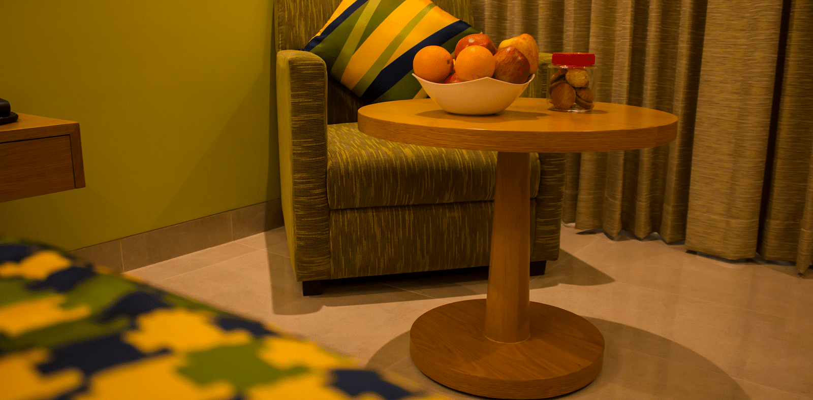 A sofa chair inside a hotel room with a table in front of it and fruits are kept on it