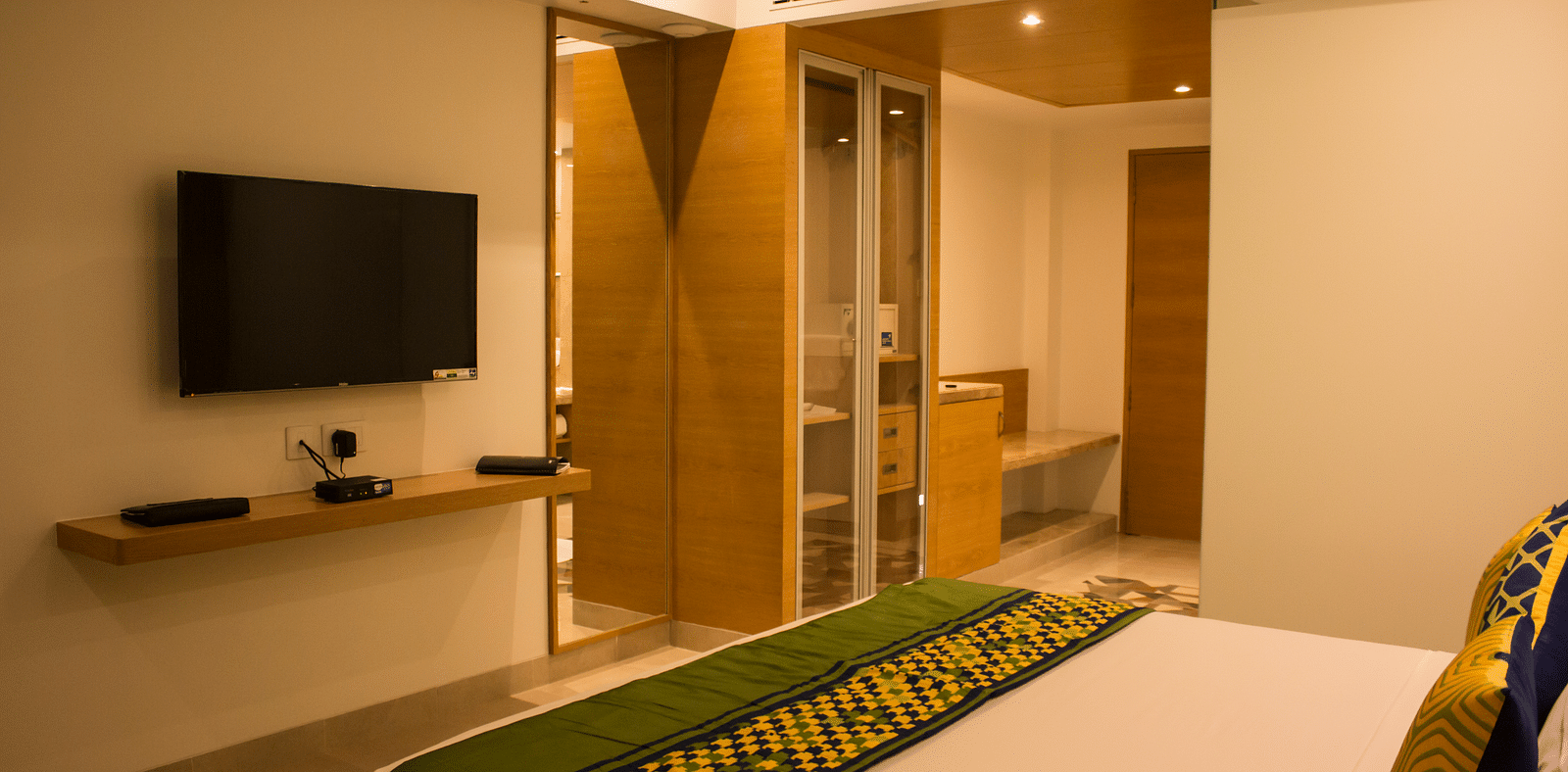Side view of a room with a bed and  pillows arranged on it  along with  a TV | Regency Tirunelveli By GRT Hotels