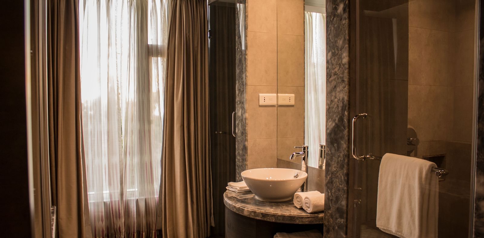 Wide view shot of a bathroom with a sink, mirrors  and towels | Regency Tirunelveli By GRT Hotels
