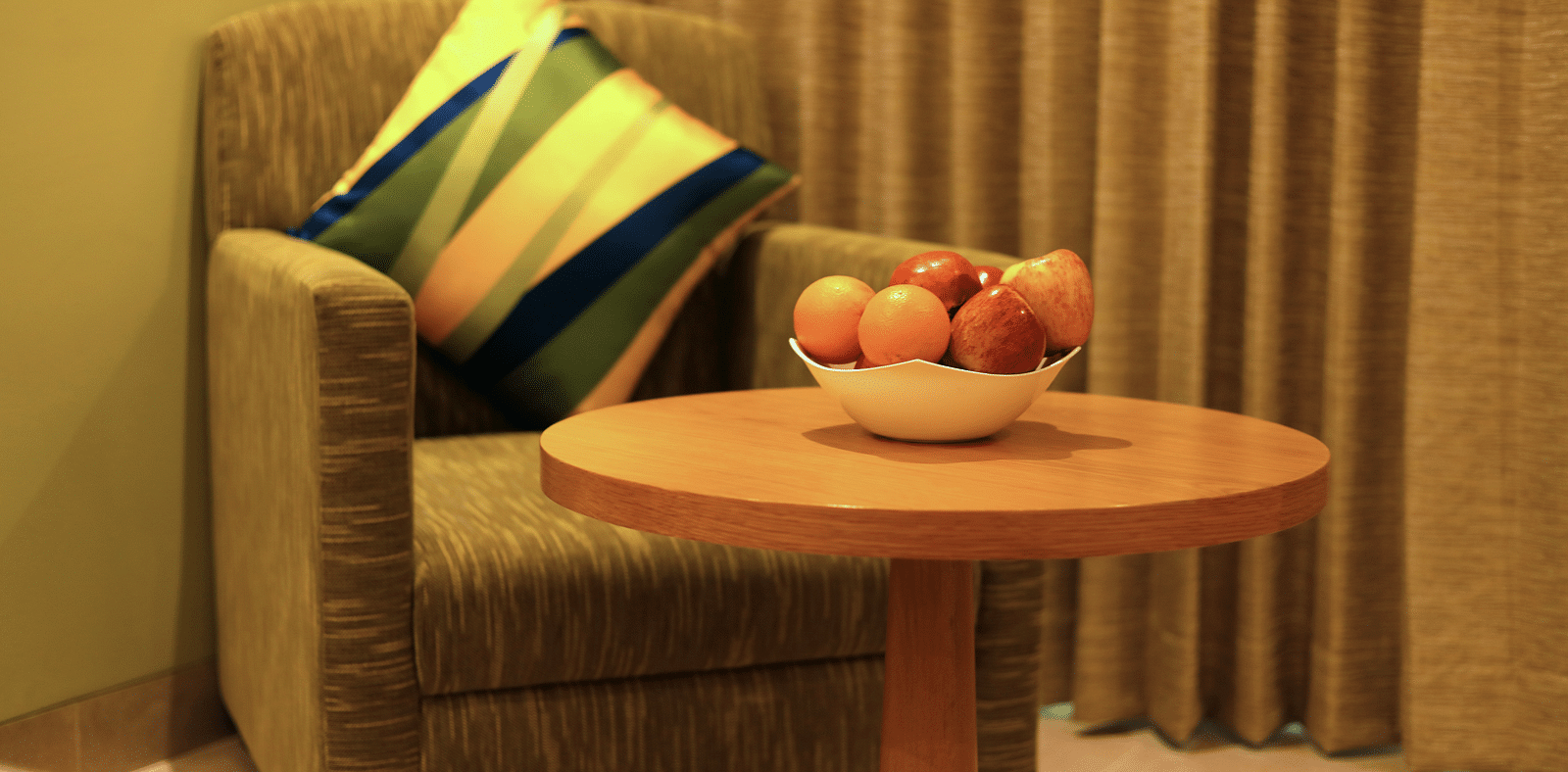Close up image of A sofa chair inside a hotel room with a table in front of it and fruits are kept on it