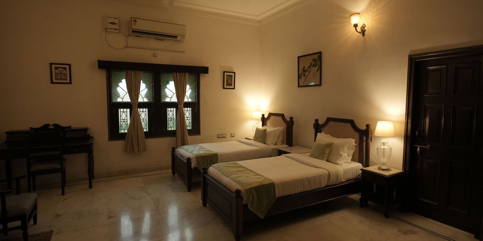  A well-lit twin room at Mahendra Niwas featuring two single beds with green and white bedding, a desk, and traditional decor.