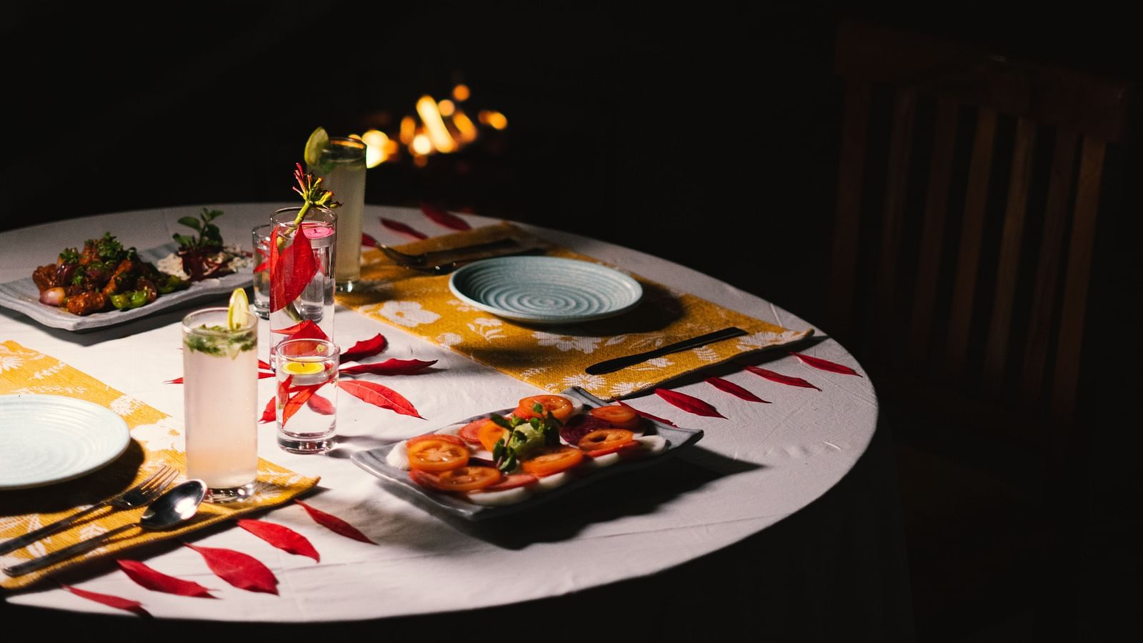 A fully set dinner table at BluSalzz Villas - The Green Roof, Bhimtal, with a cosy campfire glowing in the background.