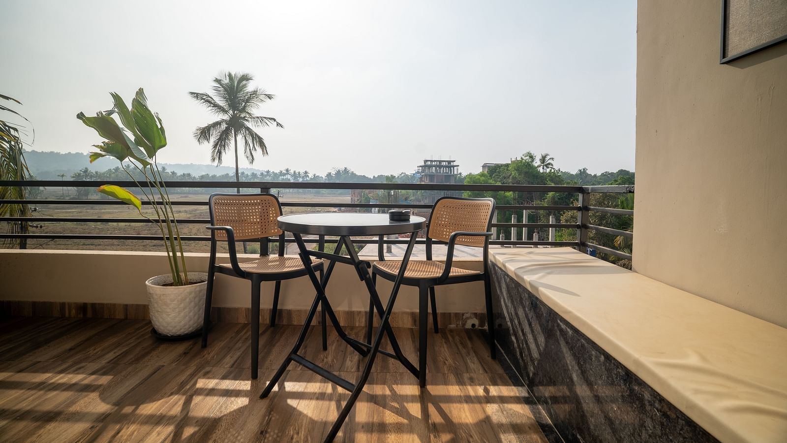 A balcony with minimalist furniture overlooking lush greenery and palm trees at Kssemya.