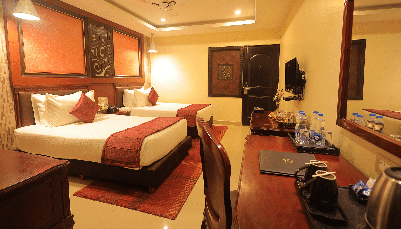 An image of a twin beds with bedside table, a set of table and chairs, flat TV screen, and AC - Sathyam Grand Resort