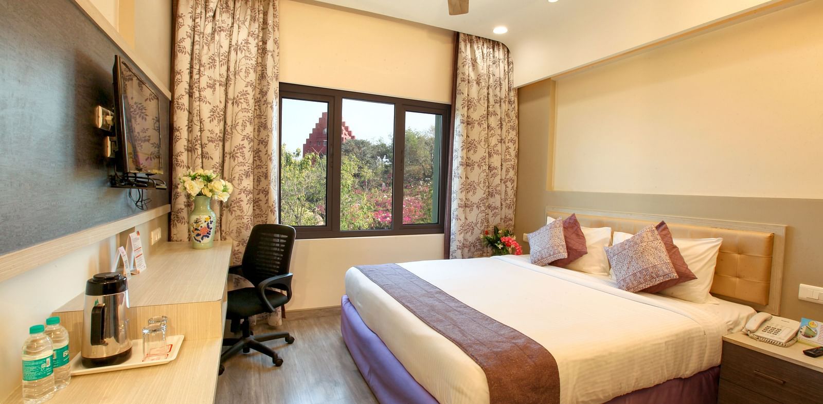 A spacious and elegantly decorated hotel room with a large window and a work area. - Tara, Comfort Hotel in Hyderabad - Ramoji Film City.
