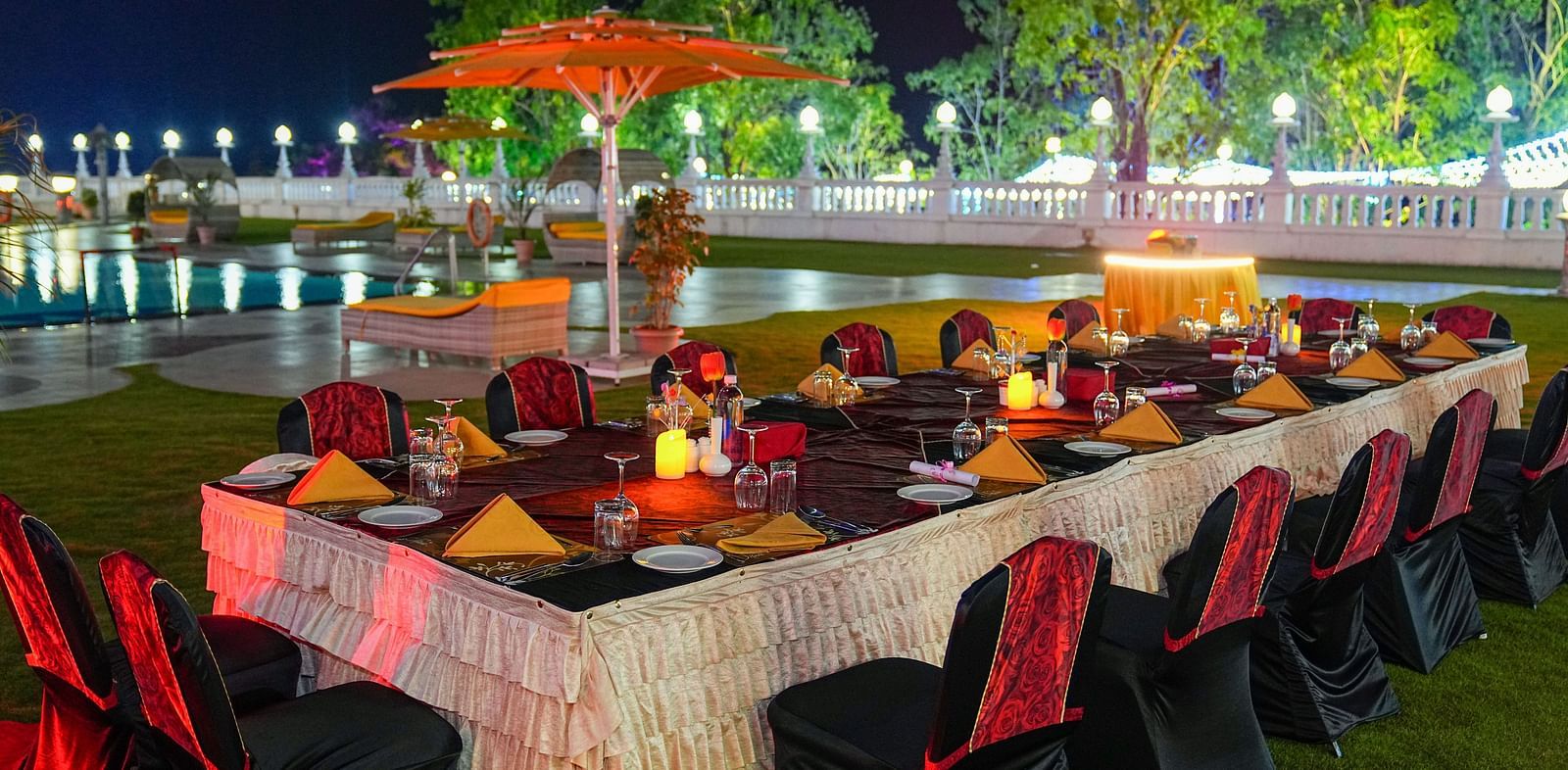 a set banquet table on a lawn with a swimming pool in the background at night - Ramoji Film City Hotels in Hyderabad 