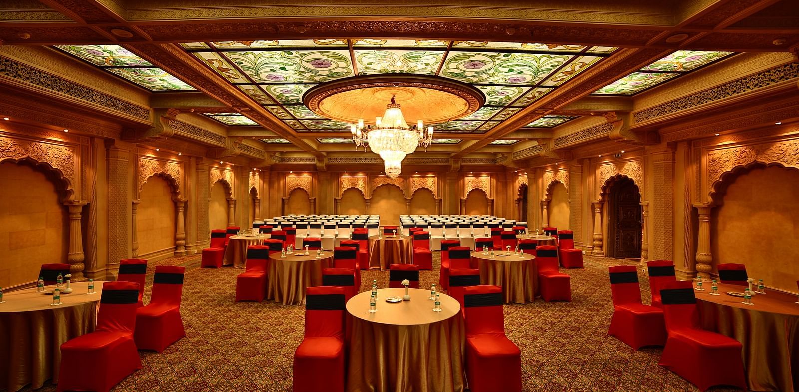 Seating arrangement in Taj Mahal Hall A grand hotel suite with an opulent red and white decor, large bed, and seating area, reflecting a traditional style at Sitara Luxury Hotel in Hyderabad near Ramoji Film City.