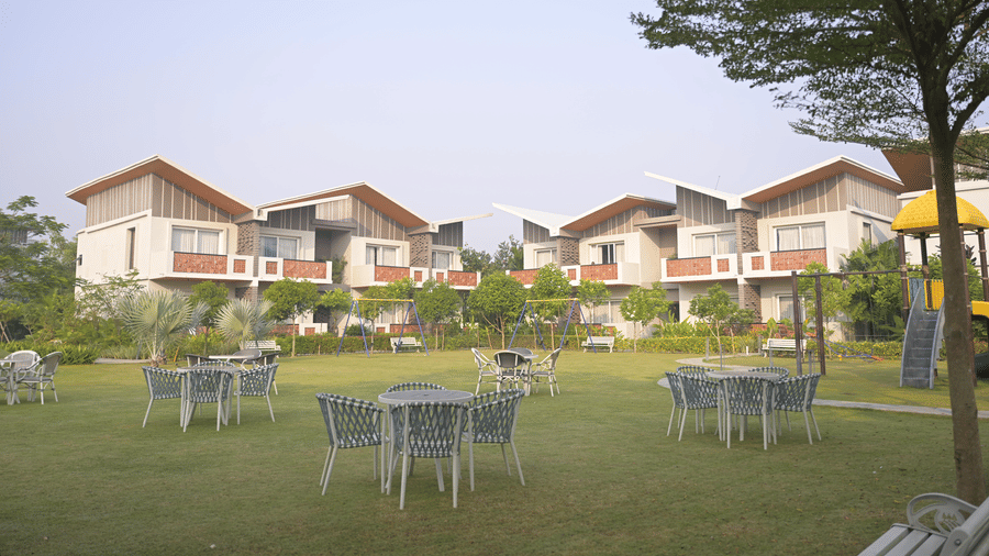 Open green lawn with white outdoor seating and rows of villas in the distance at Hotel Sonar Bangla Mayapur.