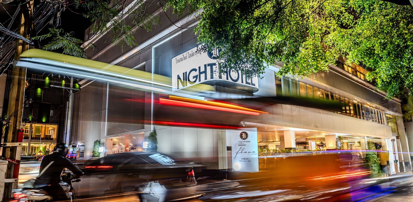 A picture showing Night Hotel Bangkok's Facade with vehicles travelling on the road.