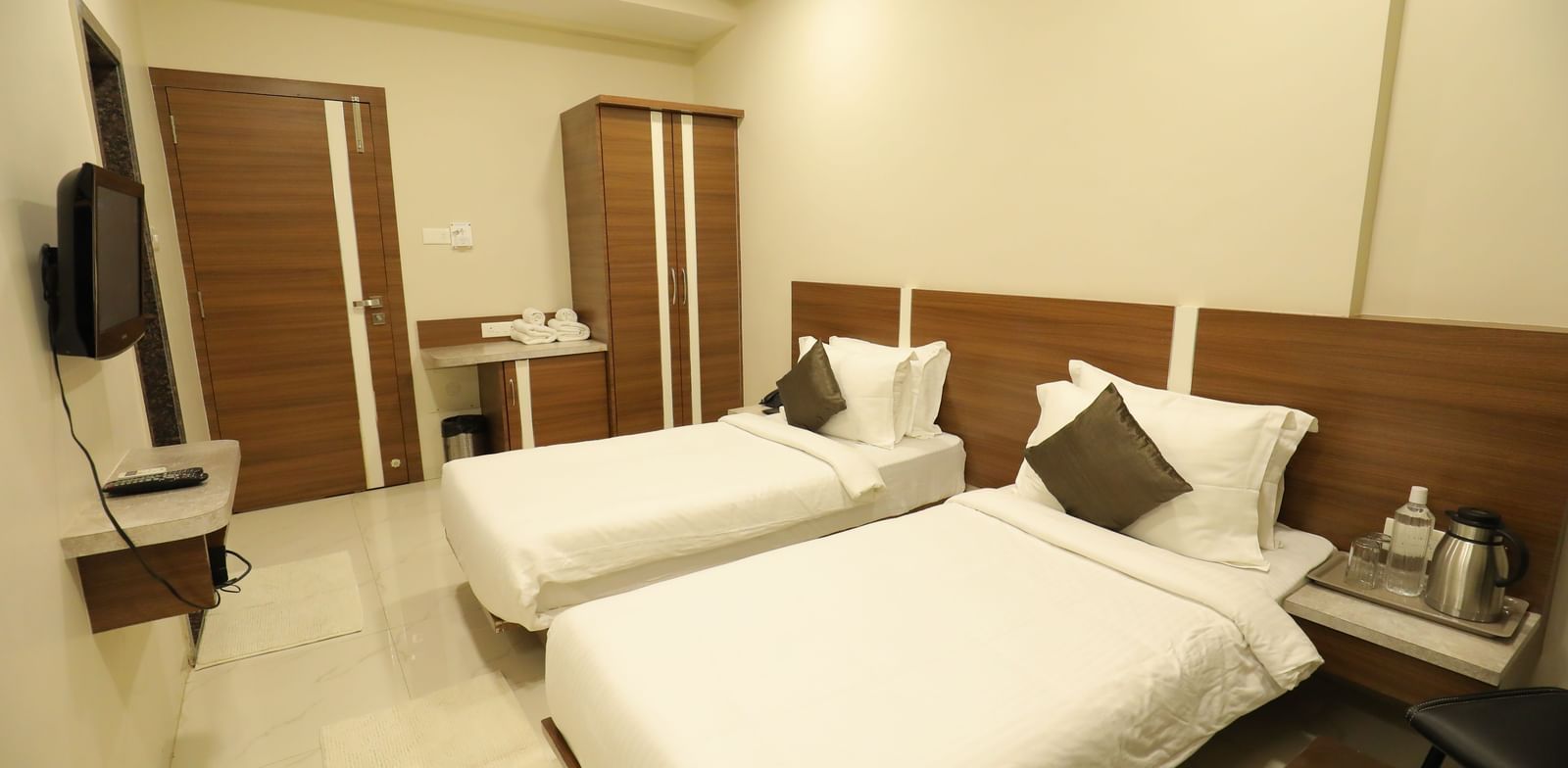 The Super Deluxe Rooms at Highland Resort feature twin beds facing a wall-mounted TV, a wardrobe, a bedside table on which a kettle is placed.
