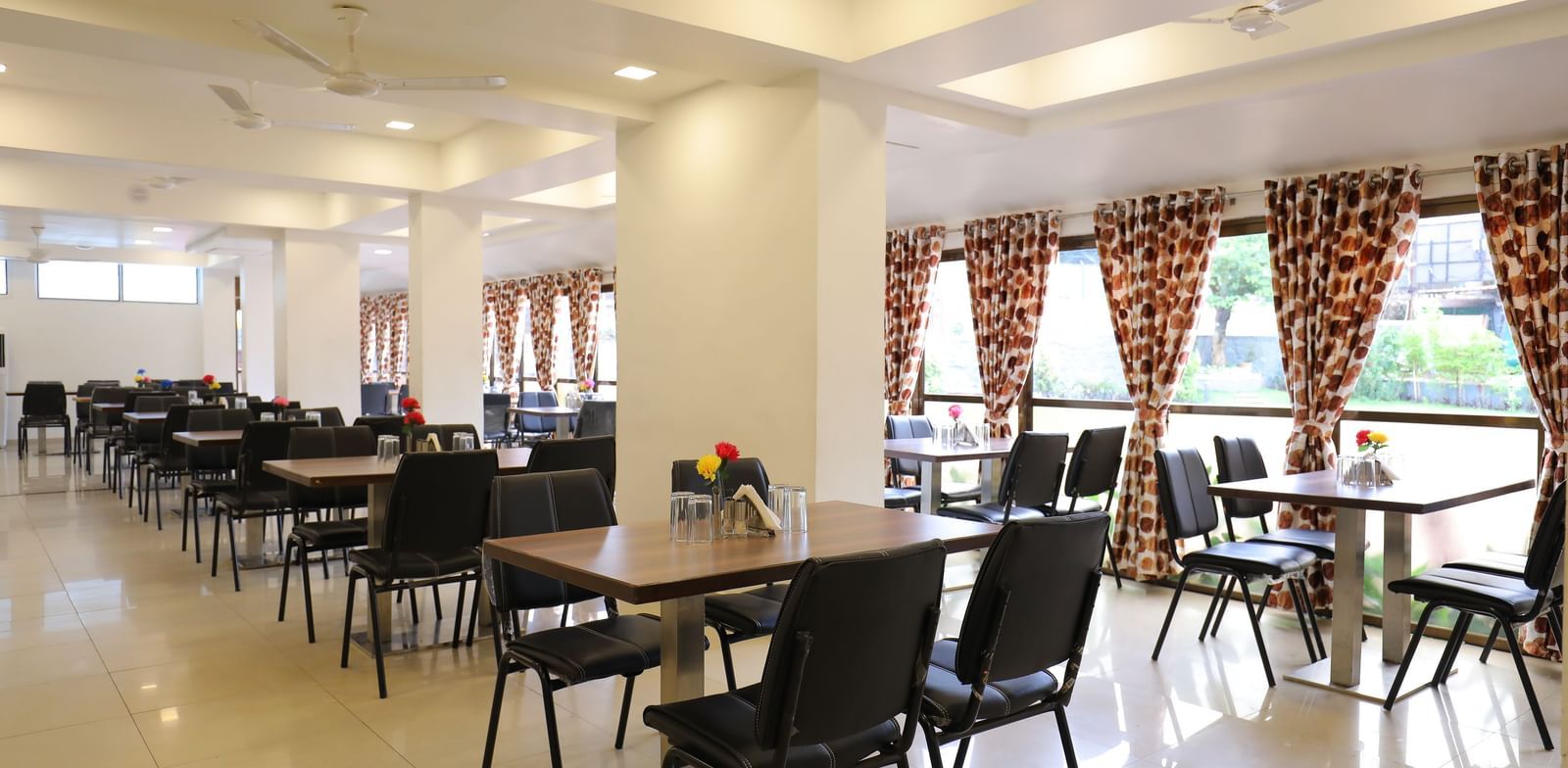 Dining tables in the spacious Darbar Restaurant that has glass windows through which natural light seeps in, at Highland Resort.