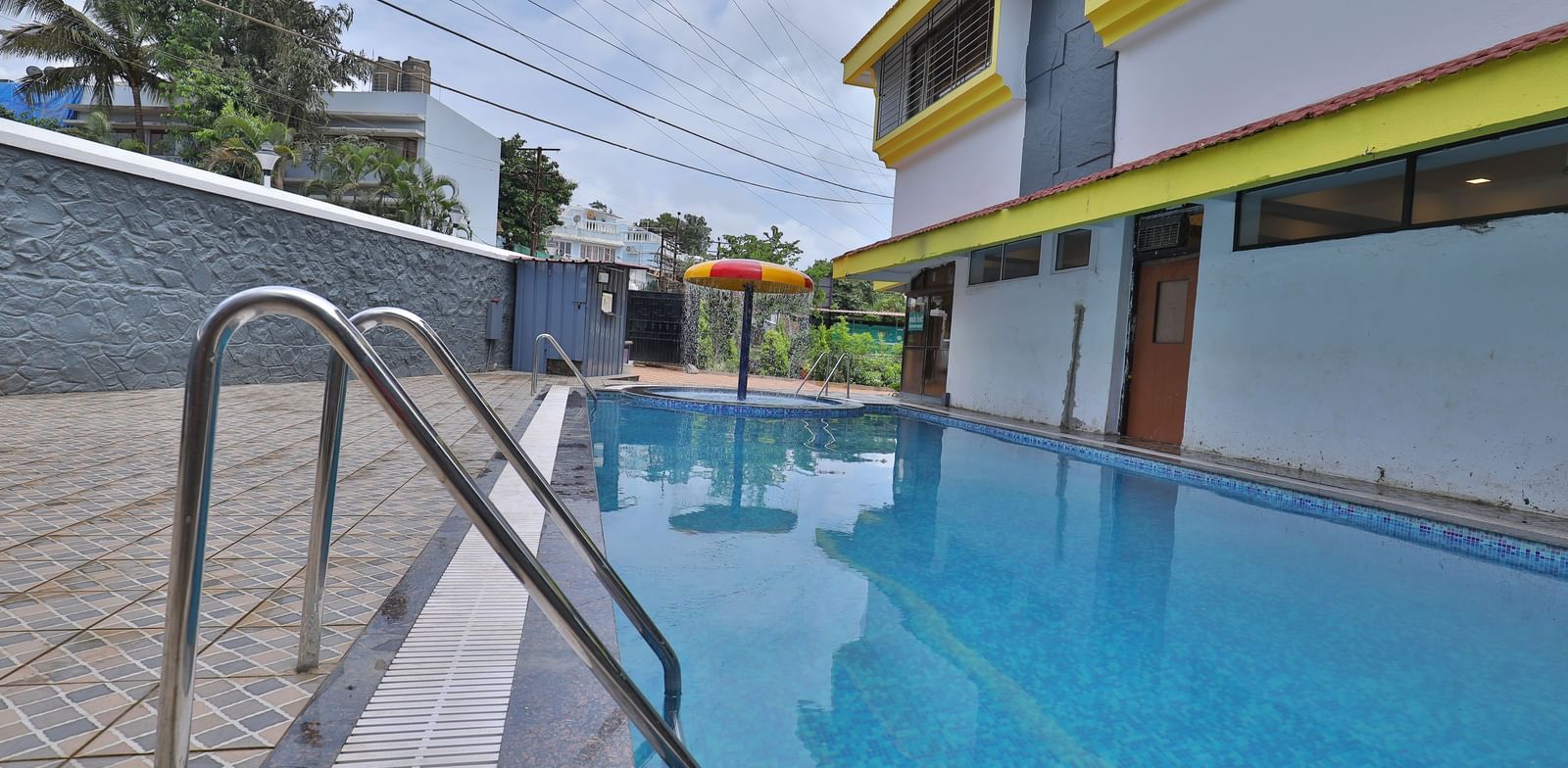 Outdoor swimming pool area with a separate circular kids’ pool featuring a mushroom-shaped water feature, pool ladders, tiled flooring at Highland Resort.