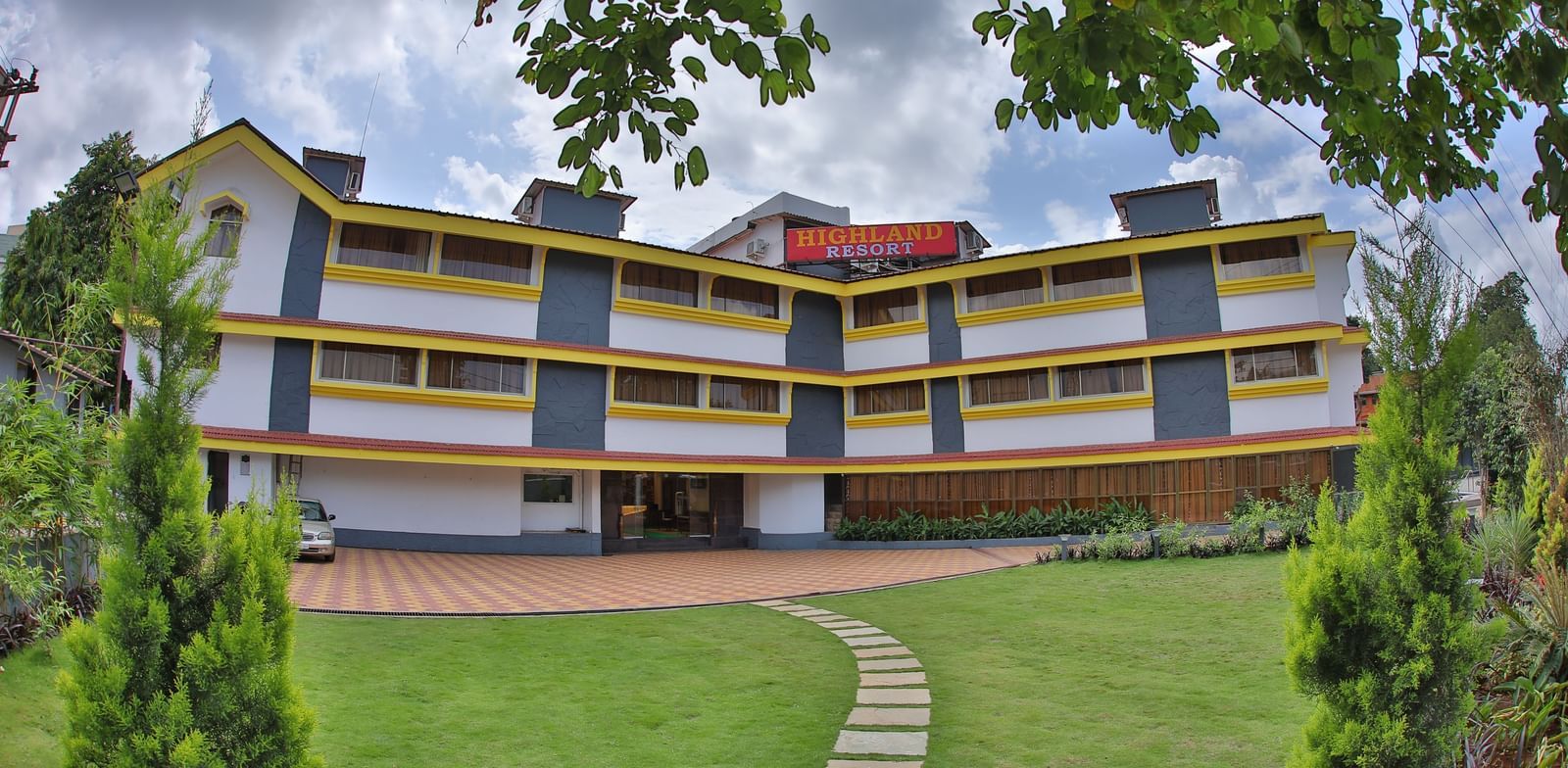 A stone pathway on a grass lawn, leading to the multi-storey Highland Resort which has a large signboard on top.