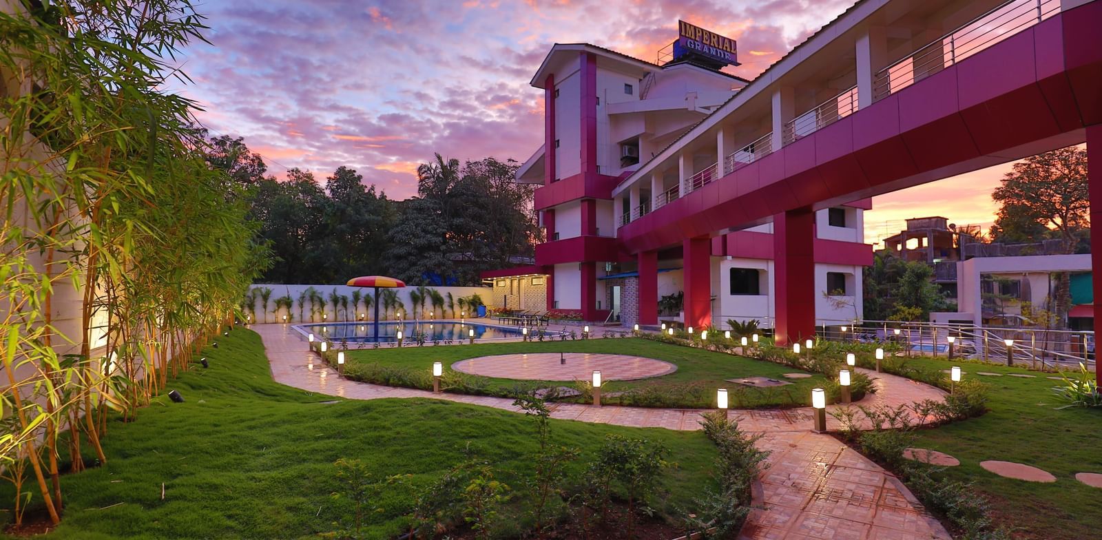 An outdoor pathway at Imperial Grande, winding through a garden area with manicured lawns and trees, leading towards a building in the distance.