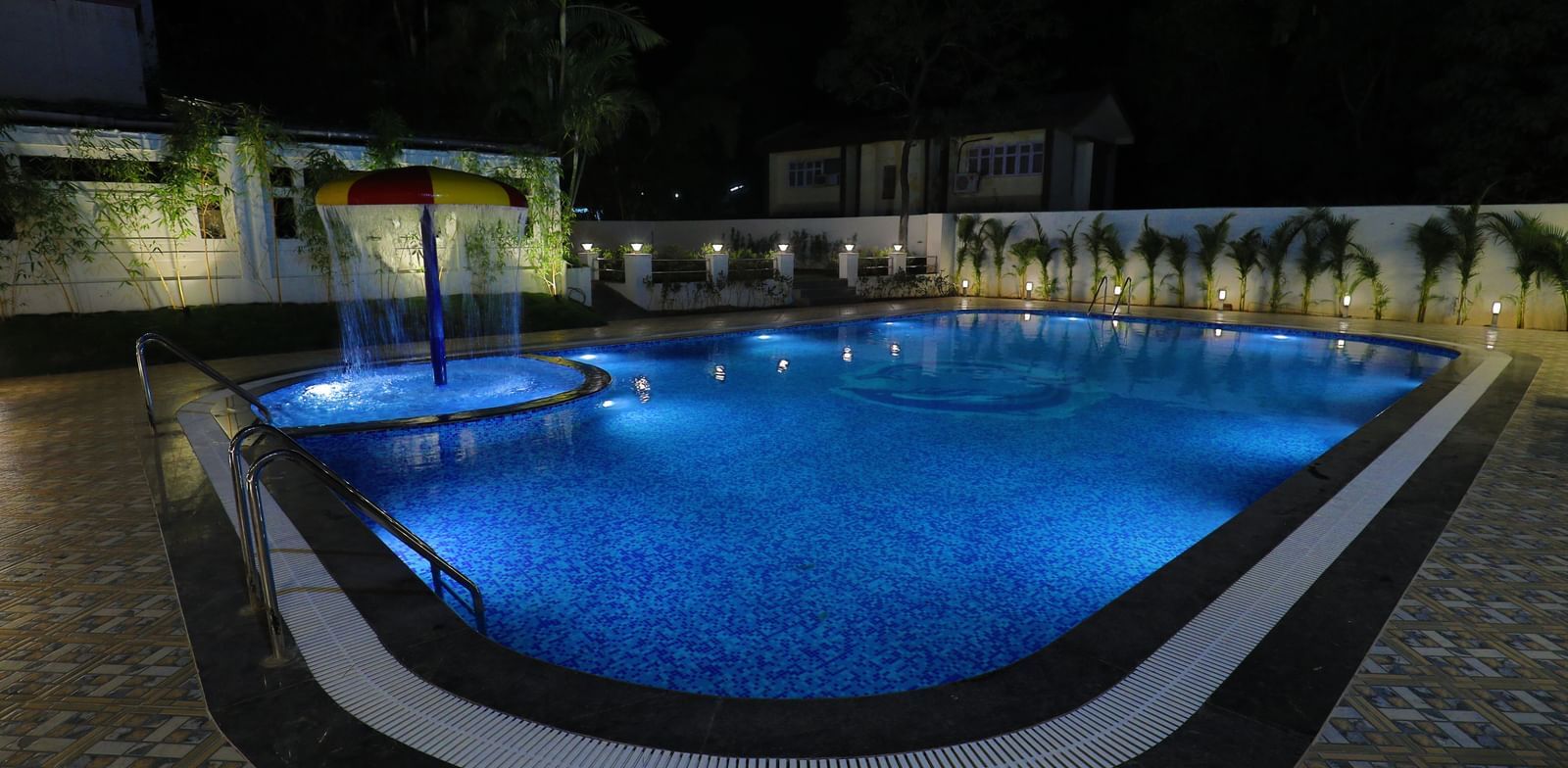 A large swimming pool at Imperial Grande, illuminated with blue lights at night, surrounded by a paved area and some seating.