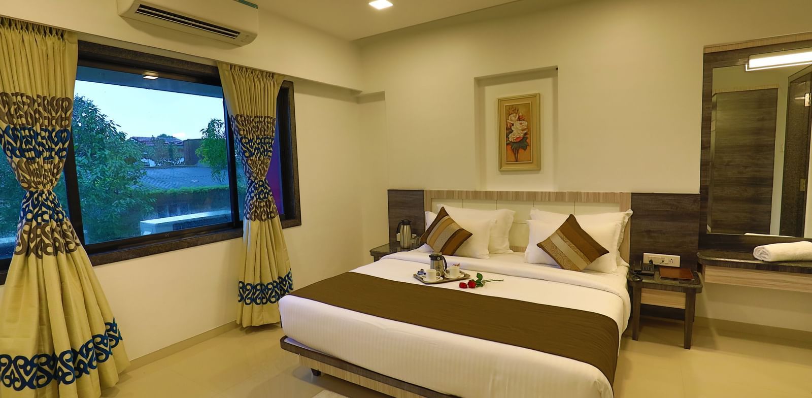 A suite at Imperial Grande with a well-made bed and a window with patterned curtains.