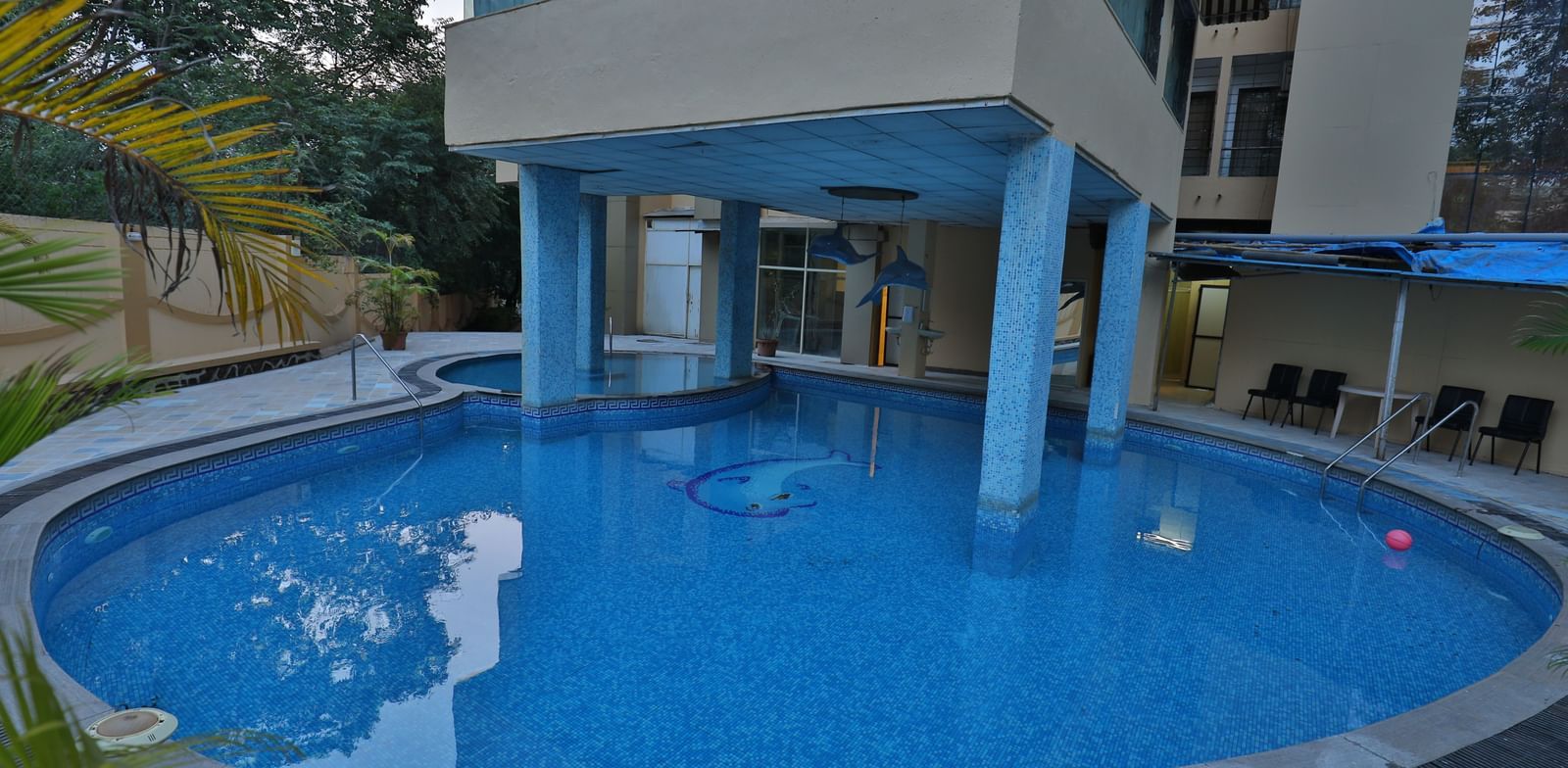 A clear view of a hotel's swimming pool, with the building's support pillars visible above the water - Retreat Heritage, Lonavala