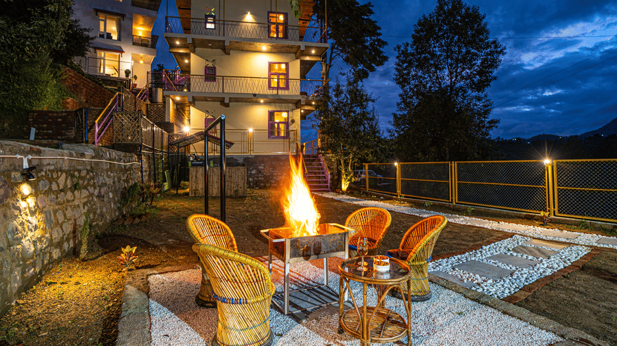 An outdoor seating area with chairs around a bonfire setup and a building in the background at Adrushya Estates, offering adventure activities in Mukteshwar