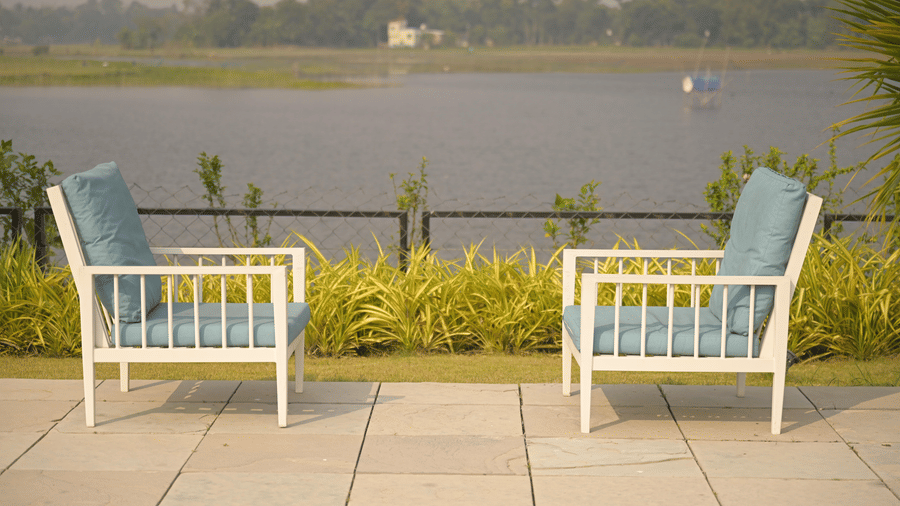 A riverside patio with 2 outdoor chairs facing the water, creating a calm retreat at Hotel Sonar Bangla, Mayapur.