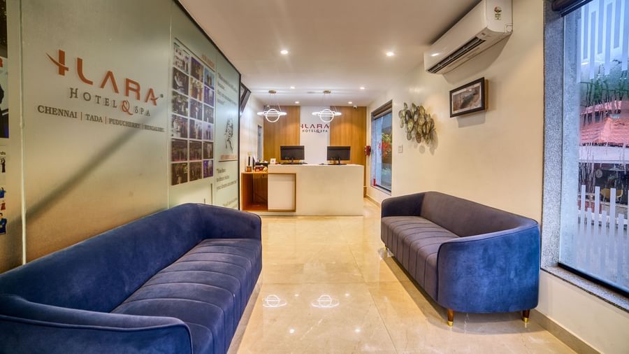 The elegant hotel lobby featuring two plush blue sofas, a minimalist reception desk, and subtle lighting, creating a welcoming atmosphere at Ilara Hotels & Spa, OMR, Chennai.