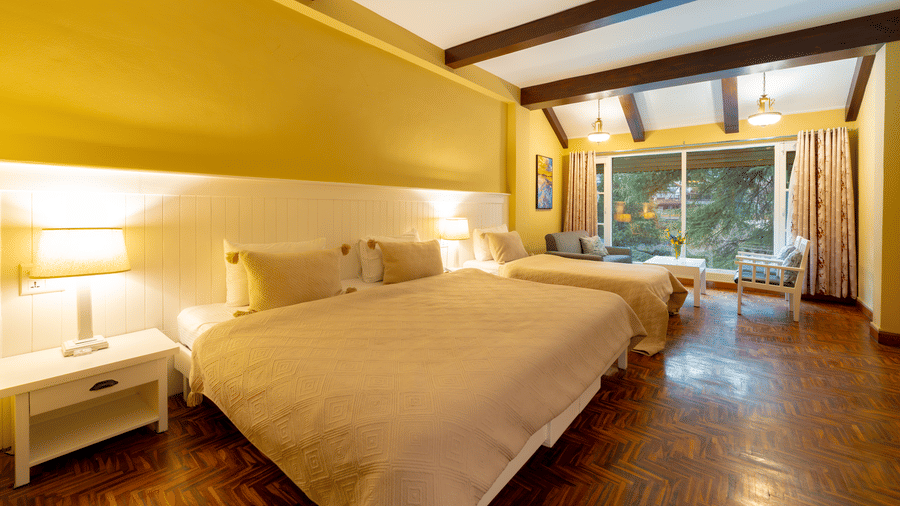 Perspective view of a deluxe family room showing the comfortable bedding and large windows overlooking the greenery - Johnson Lodge & Spa, Manali