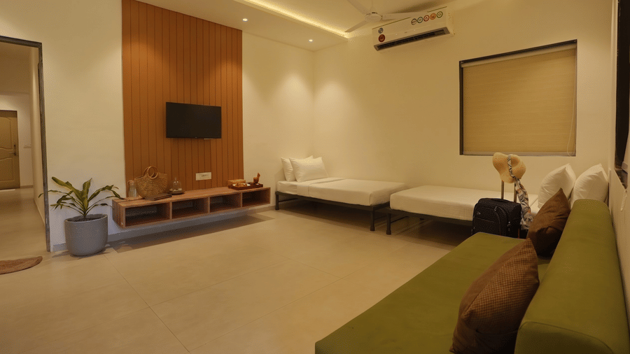 A bedroom at Oceanature Resort, Alibaug with a green sofa, 2 single beds, and a wall-mounted television on a wood-paneled wall.