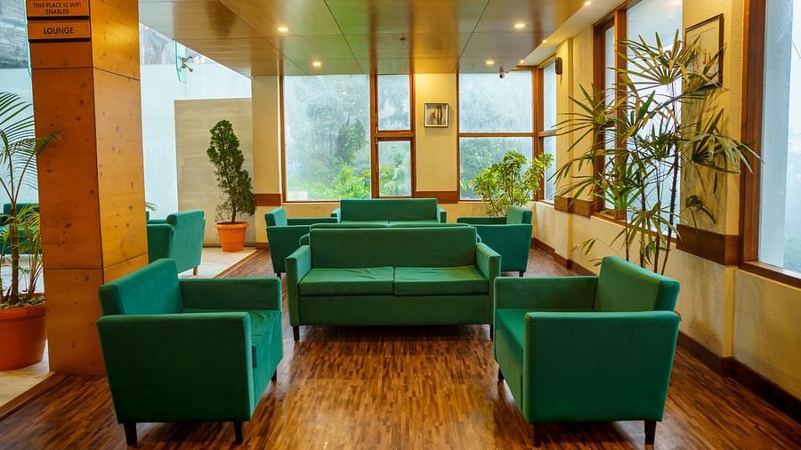 A lounge area of Orsino Spa Resort with green sofas, wooden flooring, and large windows looking out onto greenery.